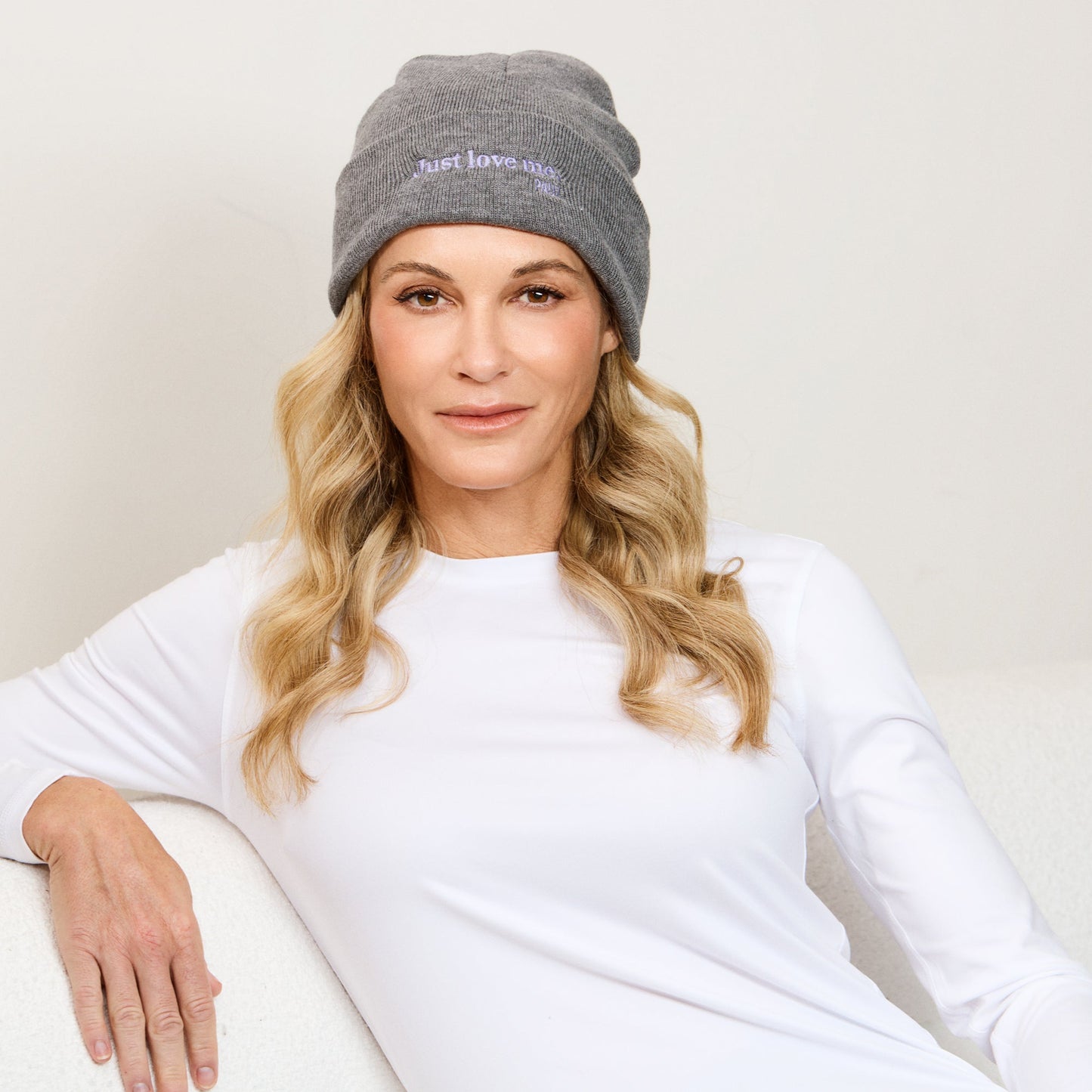 Woman wearing a beanie hat in color grey. The hat has a 'Just Love Me' message in purple.